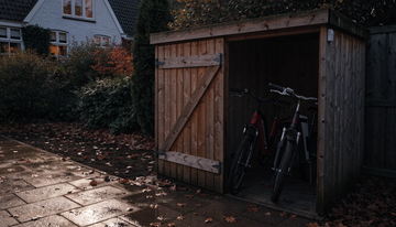 Houten schuur in de schemering met twee e-bikes en een draadloze deursensor op het kozijn